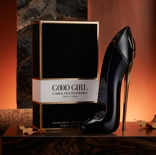 Carolina Herrera Good Girl Eau de Parfum bottle and its black box with gold trim, styled on a dark wooden surface with warm orange lighting and textured stone props.