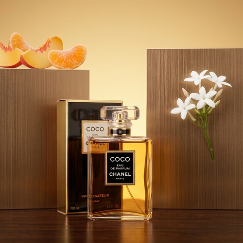 Chanel Coco Elixir perfume bottle and box displayed on a wooden surface against a warm beige background, with peach slices on a left pedestal and white flowers on a right pedestal.